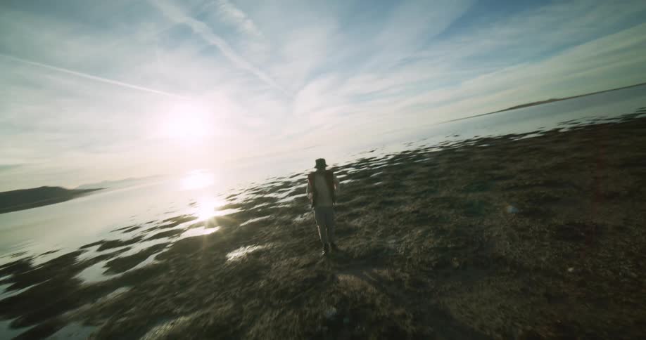 A person dances on a rocky beach nearby and a distant coastline under a sky streaked with clouds