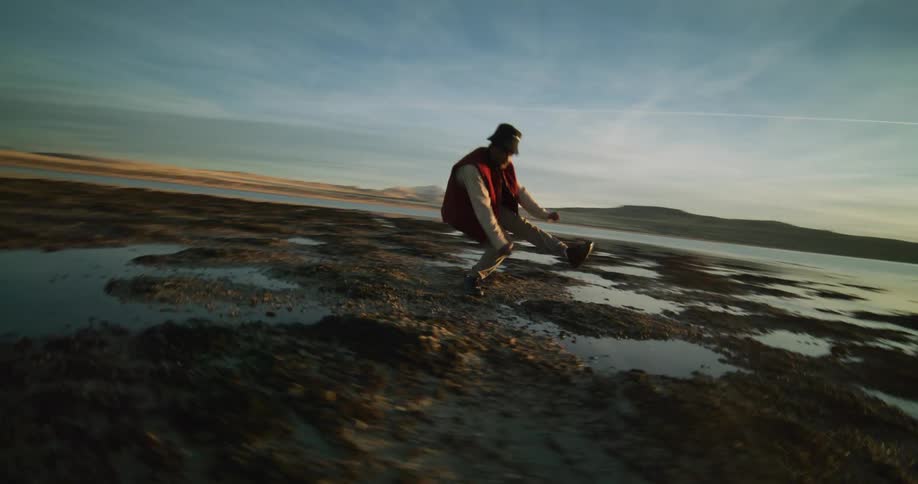 Man on the edge of a vast lake with the sun dancing on the horizon