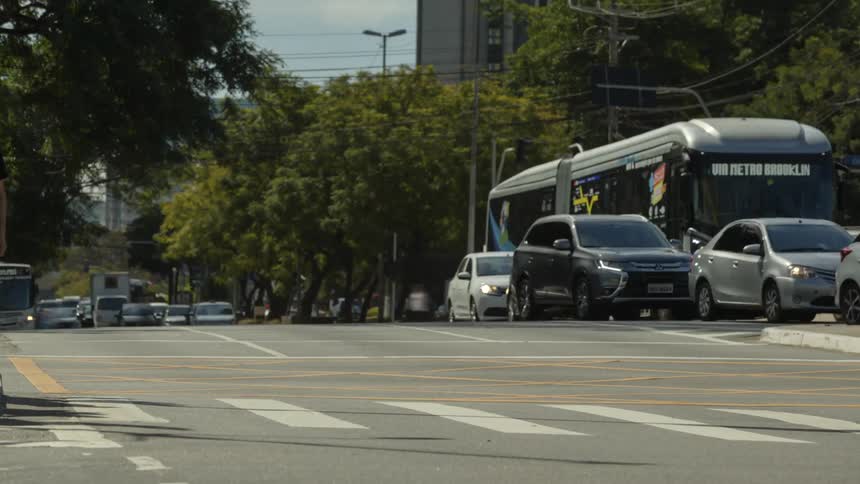 A time lapse captures a busy city street with heavy traffic and streams of pedestrians crossing