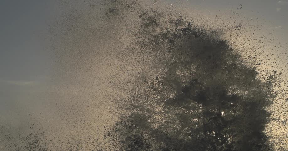 Sea spray bursts against a backdrop of a pale sky at sunset