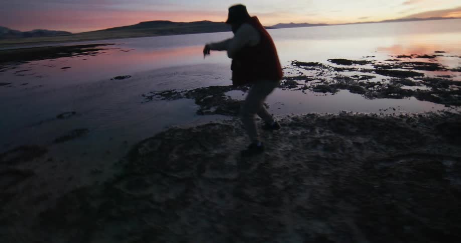Man dances in a coastal area with the colorful sky in the background during dawn