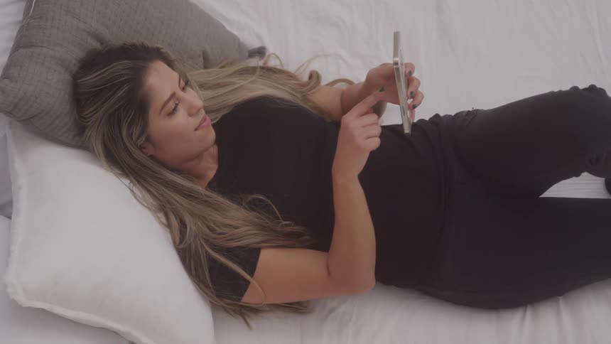 A young woman lies on her bed while scrolling on her smartphone