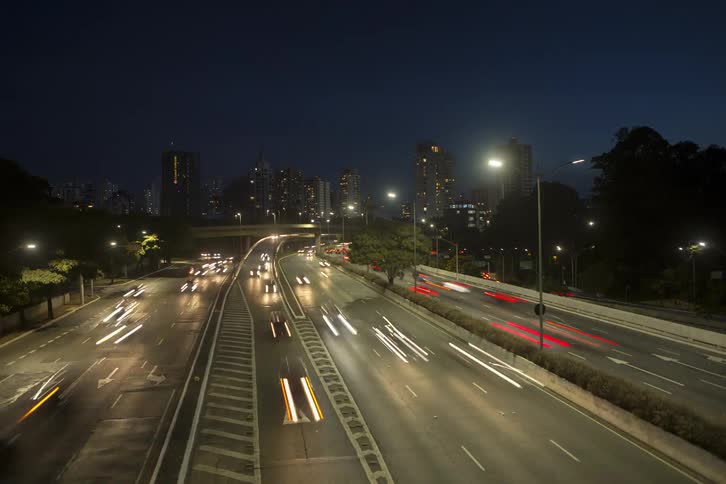 A highway stretches into the distance towards a city skyline at dusk with streaks of light from passing vehicles