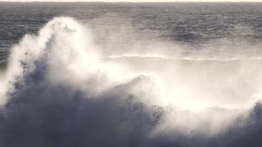 A large wave crashes against the vast surface of the ocean creating a burst of white foam