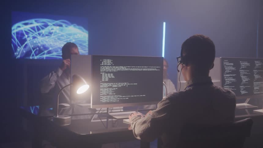 Digital environment with professionals monitoring multiple monitors displaying codes and graphics