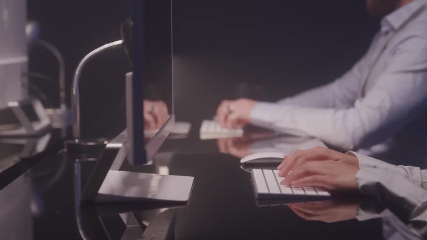 Men are typing on computer keyboards when one man takes a sip of coffee from a mug