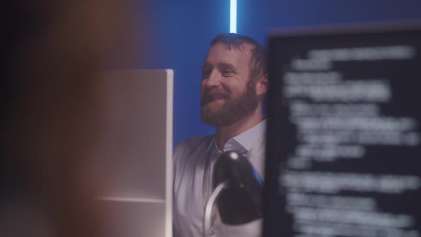 A bearded man is smiling while talking online on the computer