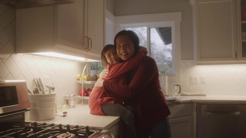 A mother and daughter hug in the kitchen of a house