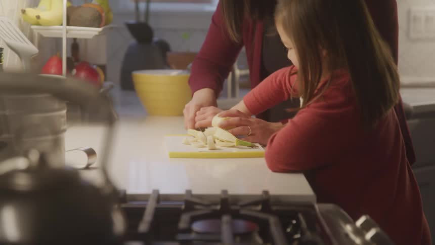A woman is helping a little girl chop vegetables in a kitchen