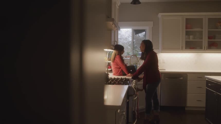A woman is standing in a kitchen talking to a girl who is sitting on the counter