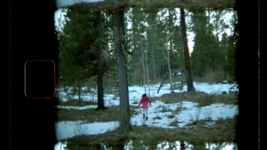 A girl in a red jacket walking through a snowy forest landscape framed by tall trees