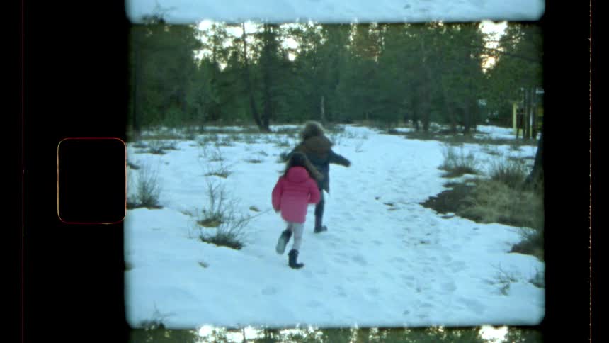 Two girls run excitedly out into the snow in a forest