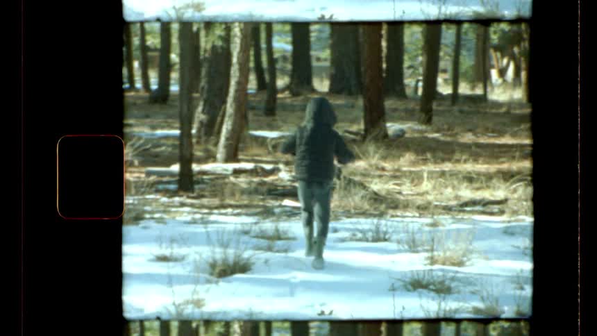 A boy waves his arms around him as he walks on the snow in a forest