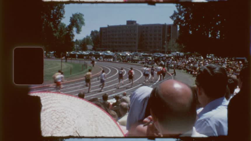 Several athletes preparing to start running on a track with a curve and a large audience watching
