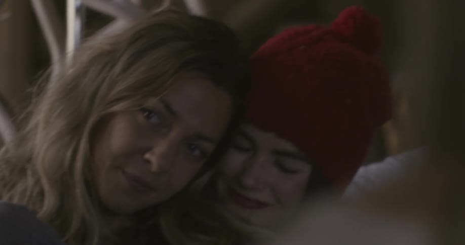 Two women laugh and lean on each other while sitting down
