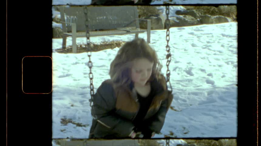A child wearing a winter coat is sitting on a swing in a snowy playground