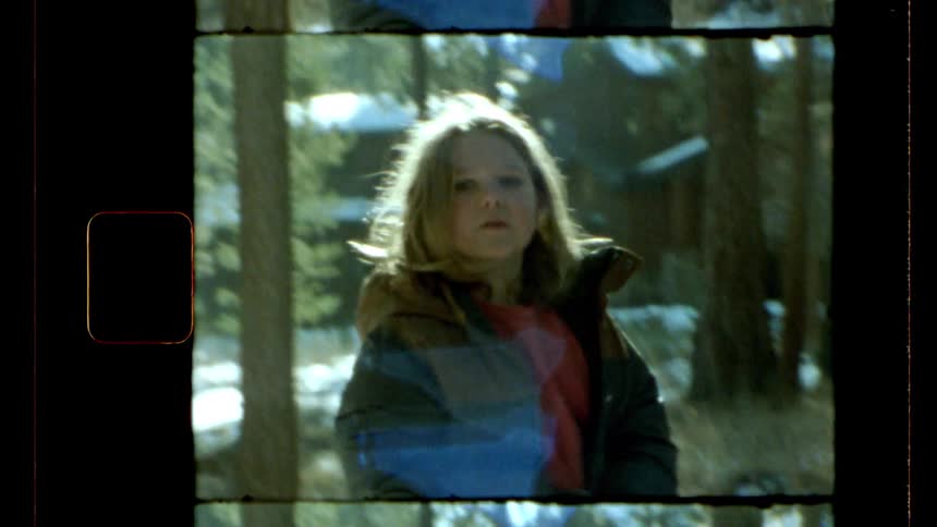 A girl in winter clothes crouches on the snowy ground of a forest beginning to stand up