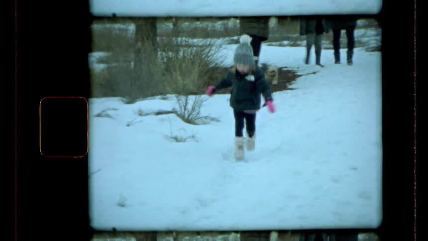 A child in winter attire walks on a snowcovered path surrounded by trees with other people visible in the distance