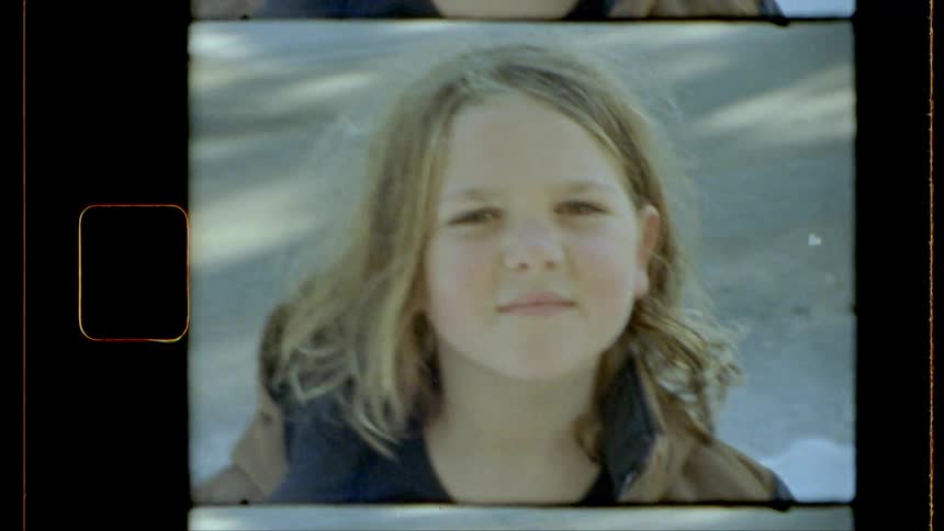 Framed within an analog film strip with noticeable grain a child with fair hair looks straight into the lens their gaze direct and engaging capturing a spontaneous moment in a portrait style