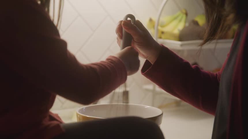 Two children use a whisk to mix ingredients in a bowl within a kitchen setting