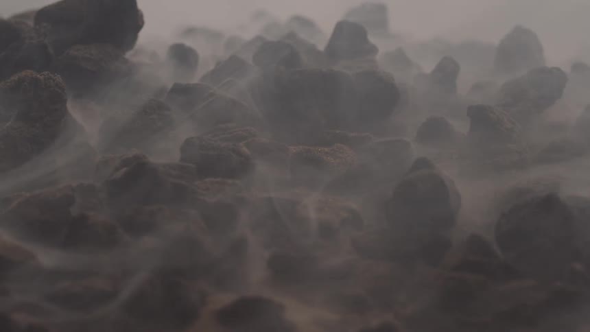 Some stones on the ground and a small white smoke passing between them