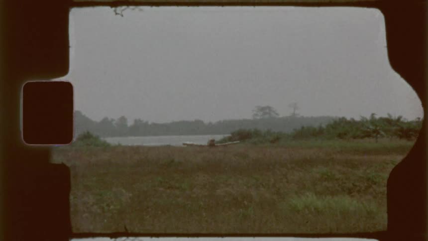 A small aircraft flying low over a field of tall grass with the film supply logo visible in the distance