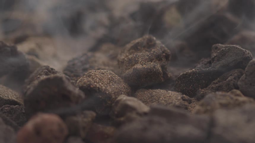 A rugged dark rocky surface with light mist or steam gently rising suggesting geothermal activity or heat
