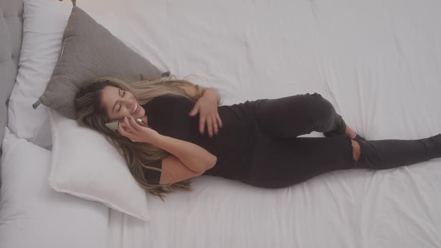 Woman is lying in bed smiling while talking on the phone