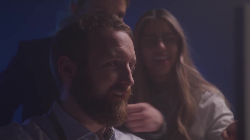 Man smiles as he sits while two women in the background watch