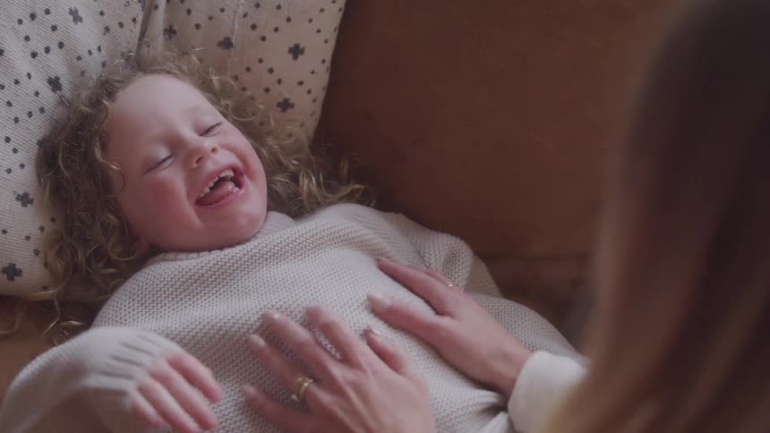 A little girl laughs as her mom tickles her
