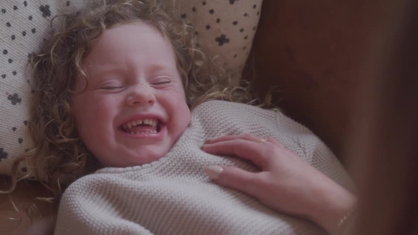 Little girl smiles as she lies down with an adult hand tickling her chest