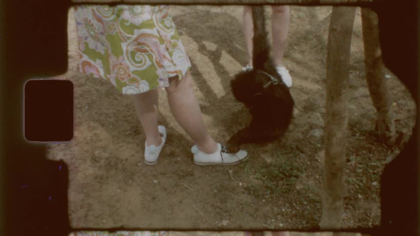 A monkey plays with the shoelaces of a woman standing outdoors captured on vintage film