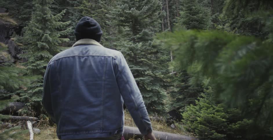 Man wearing a coat and hat walks through the woods