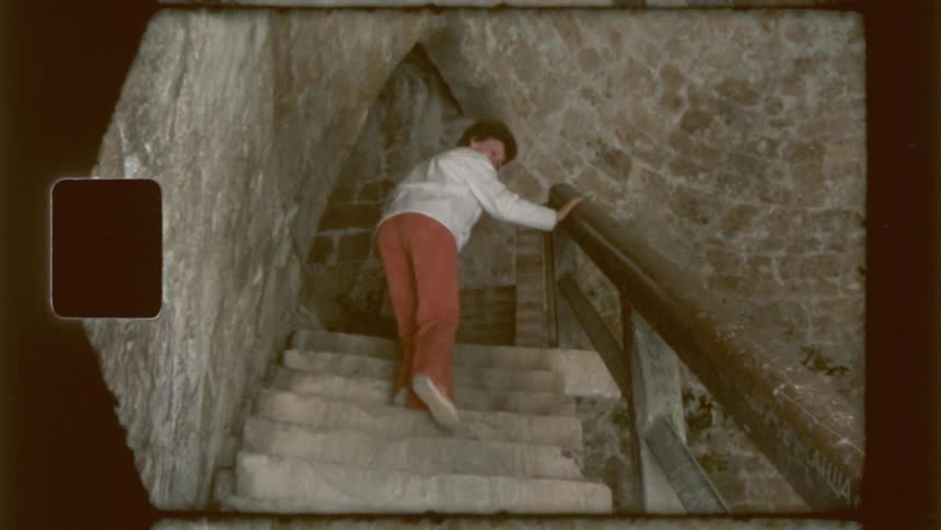 A boy waves and looks back as he climbs a staircase in a castle