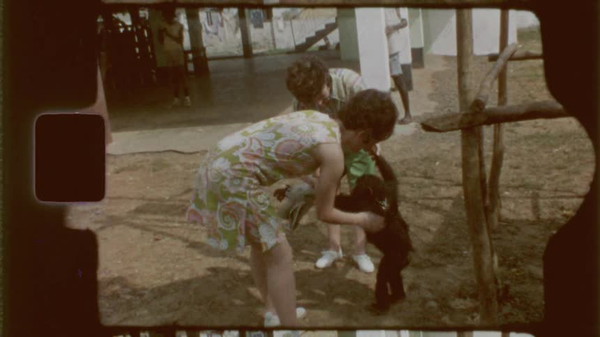 Two women clean a pet chimpanzee in a rural setting captured on vintage film