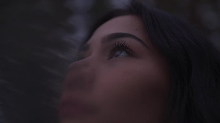 A blurry close up of the face of a woman looking up on a forest at dusk