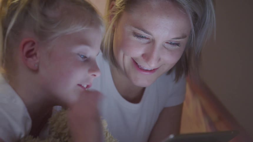 Mother next to her little daughter interacting together with a tablet