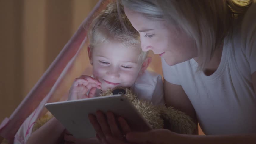 Mother lying next to her little daughter and using a tablet