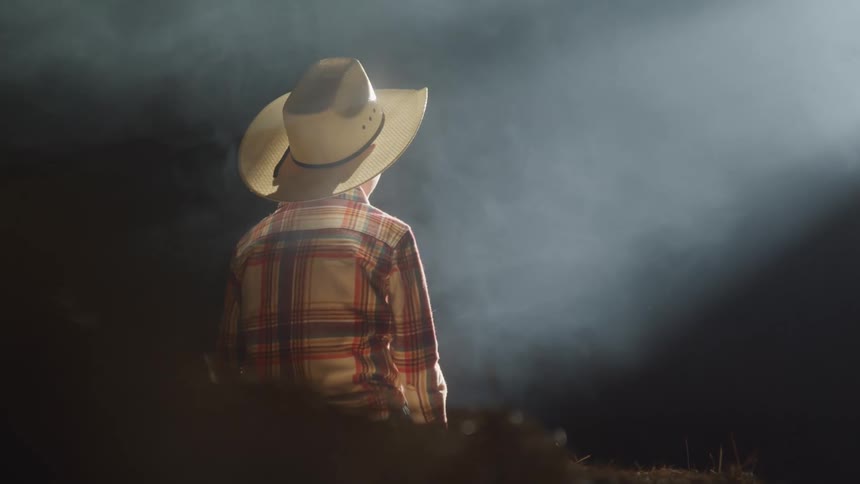 Boy in cowboy outfit sitting in a barn