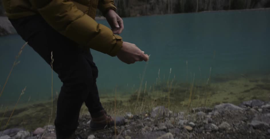 A man is picking up some rocks on a hill to throw in the lake