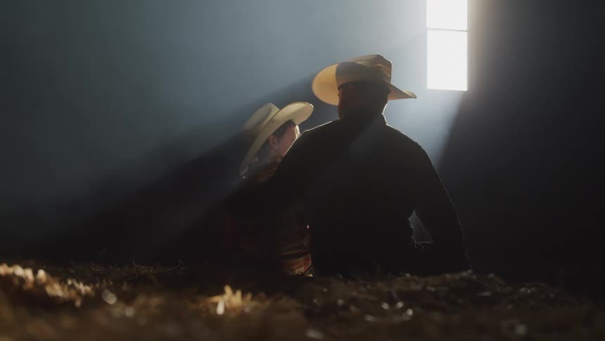 Father and son in cowboy outfits sitting with a beam of light coming through a nearby window