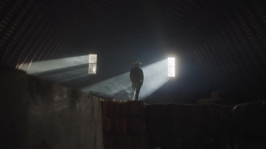 Cowboy standing in a barn with low lighting