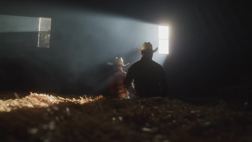 Father and son sitting in a barn next to a window
