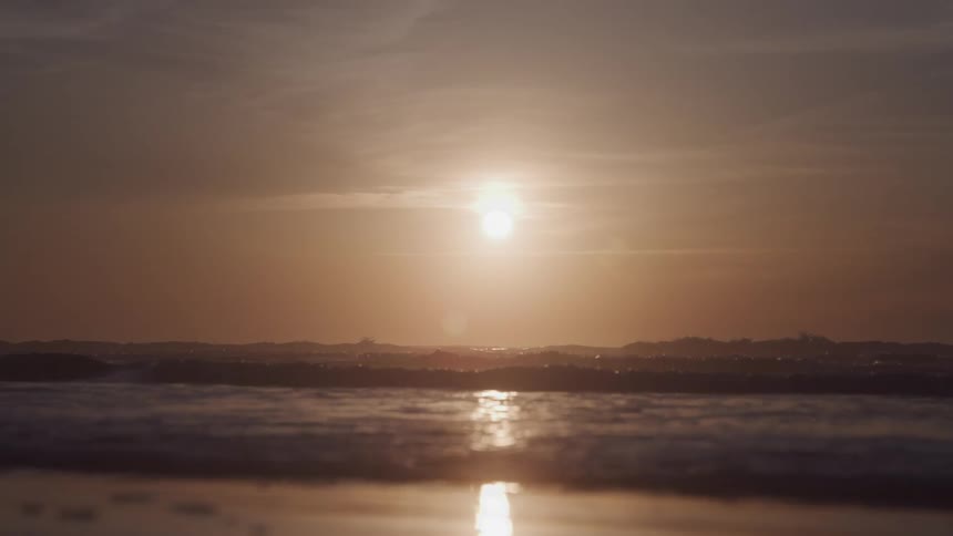 Landscape of a calm beach with the sun on the horizon