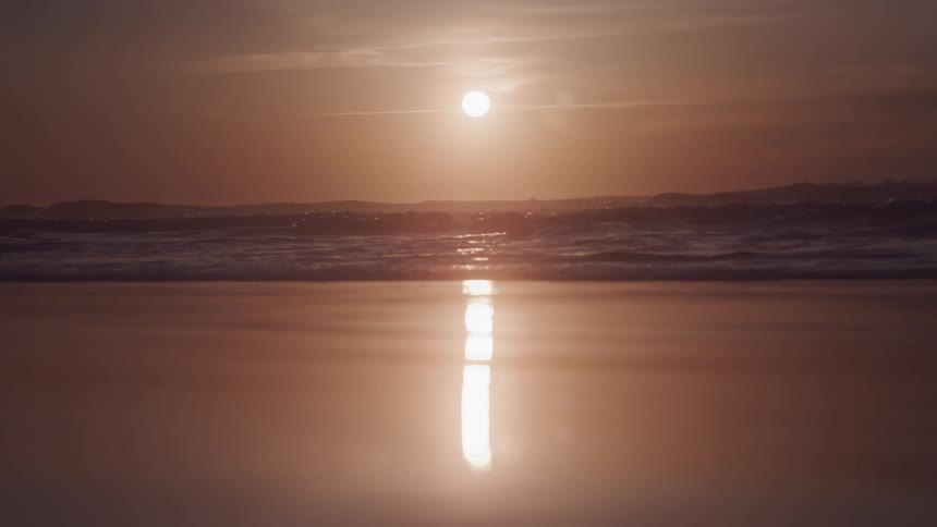Landscape of a beach with the orange sun on the horizon