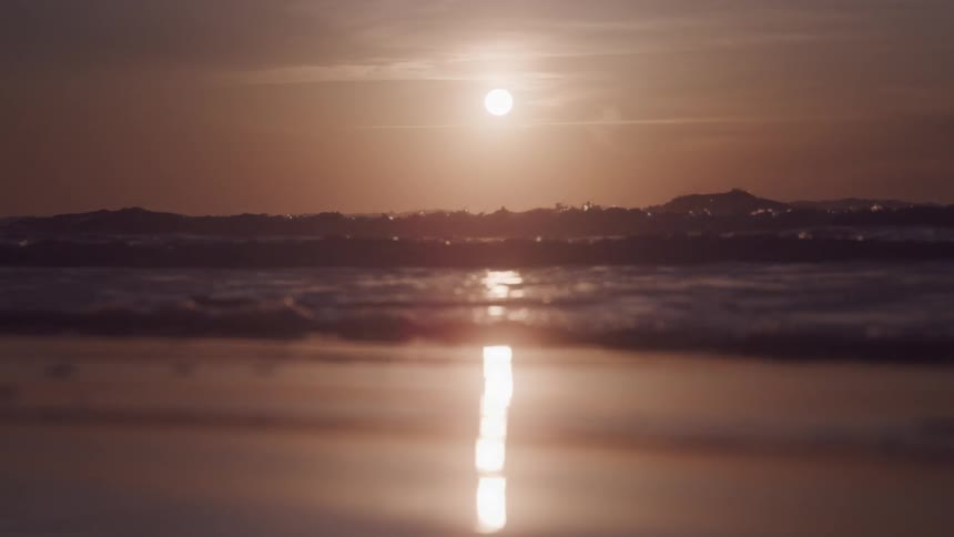 Landscape of calm waters on a beach with the sun on the horizon