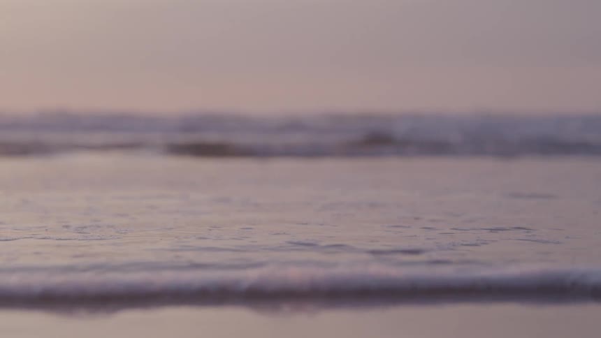Water on a beach calms down with foam reaching the shore of the sand