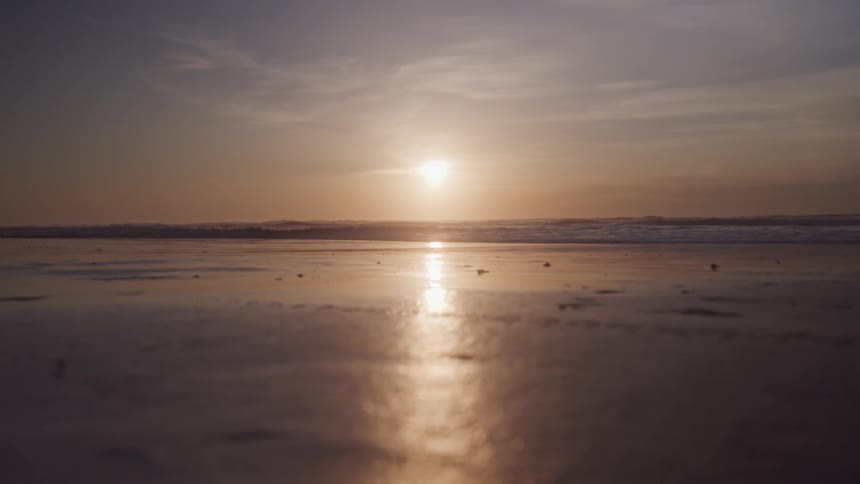 A sunset bathes the beach in golden light with the suns reflection shimmering on the wet sand