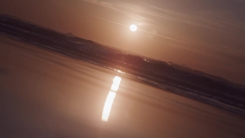 The suns reflection casts a strong diagonal line across the wet sand of a beach with the ocean waves in the background
