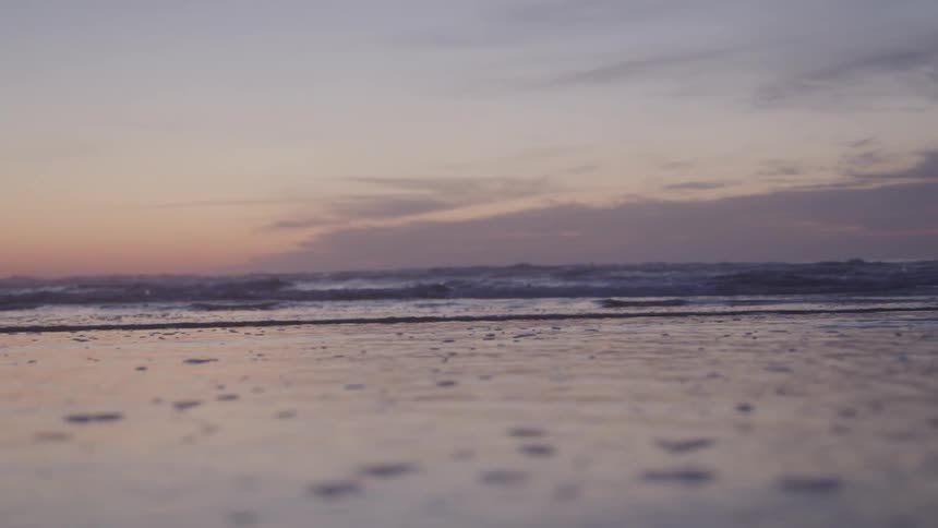 The ocean meets the sand under a dusky sky at the end of the day